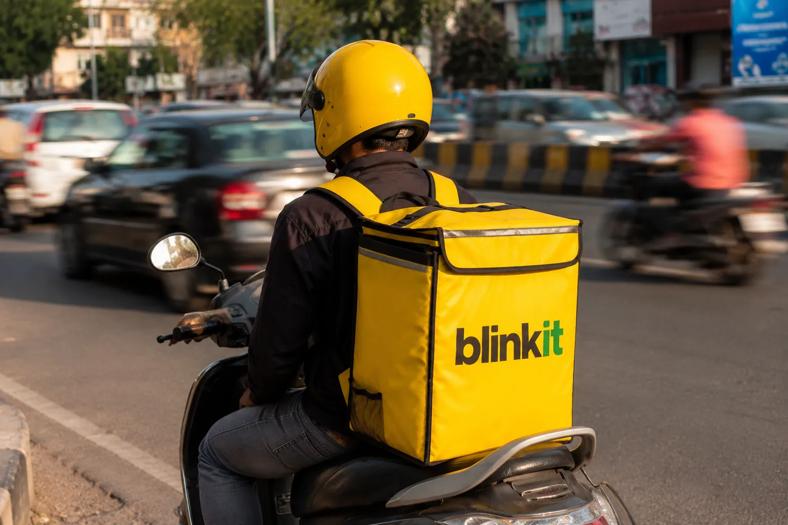 Blinkit delivery rider on a scooter in city traffic